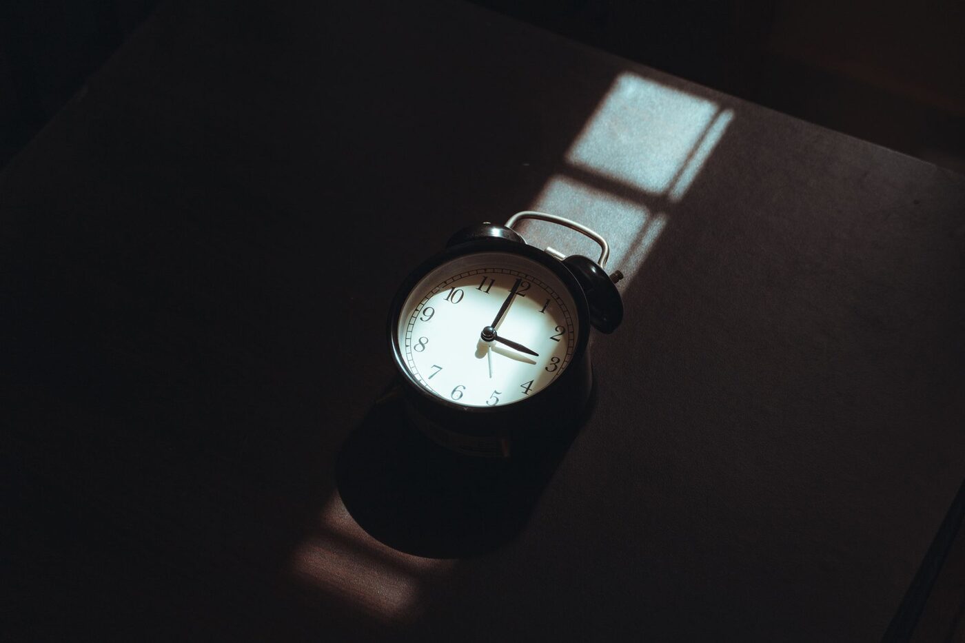 Réveil mécanique posé sur une table de nuit dans une chambre sombre
