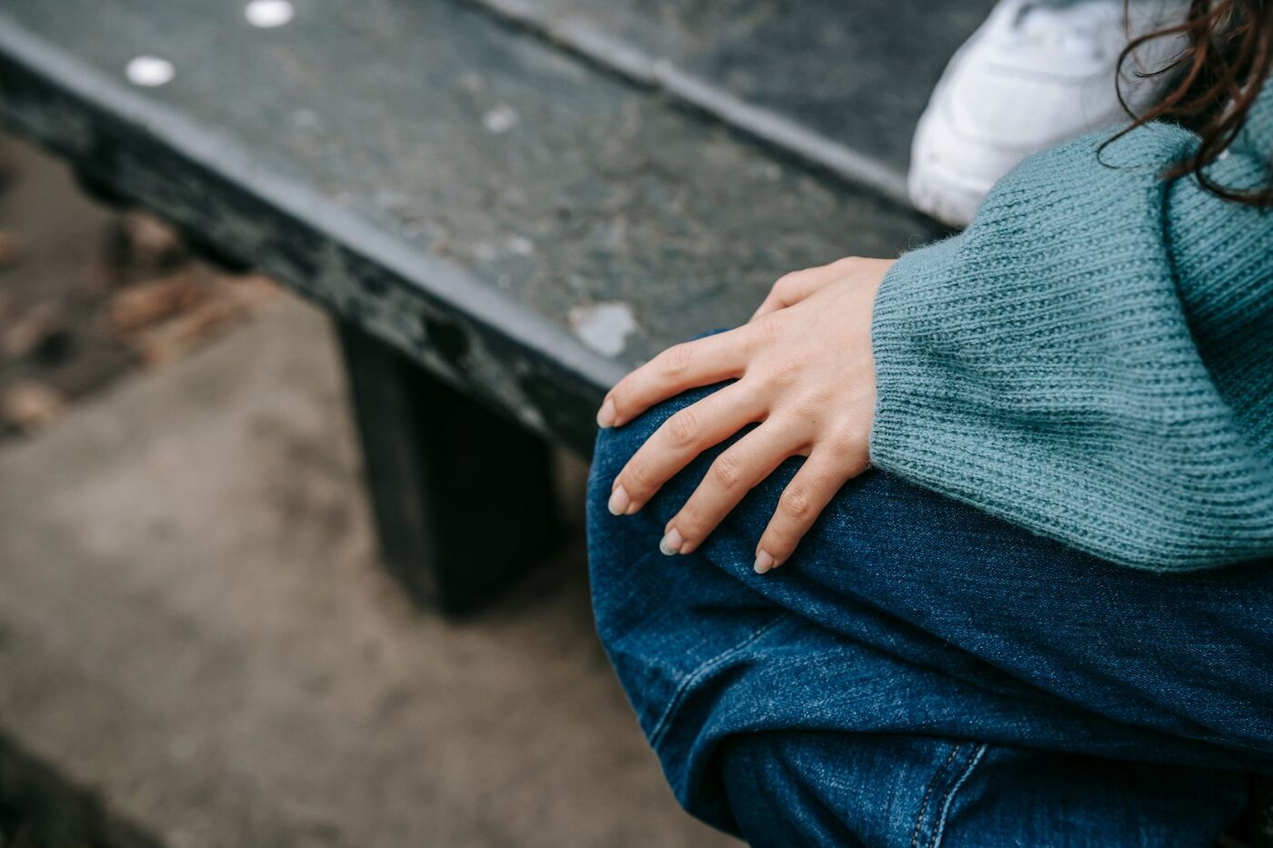 Mains posées sur un genou, pull en laine vert d'eau, personne assise sur un banc