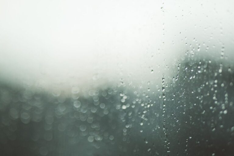 Gouttes de pluie sur une vitre, arrière-plan vert flou, lumière grise