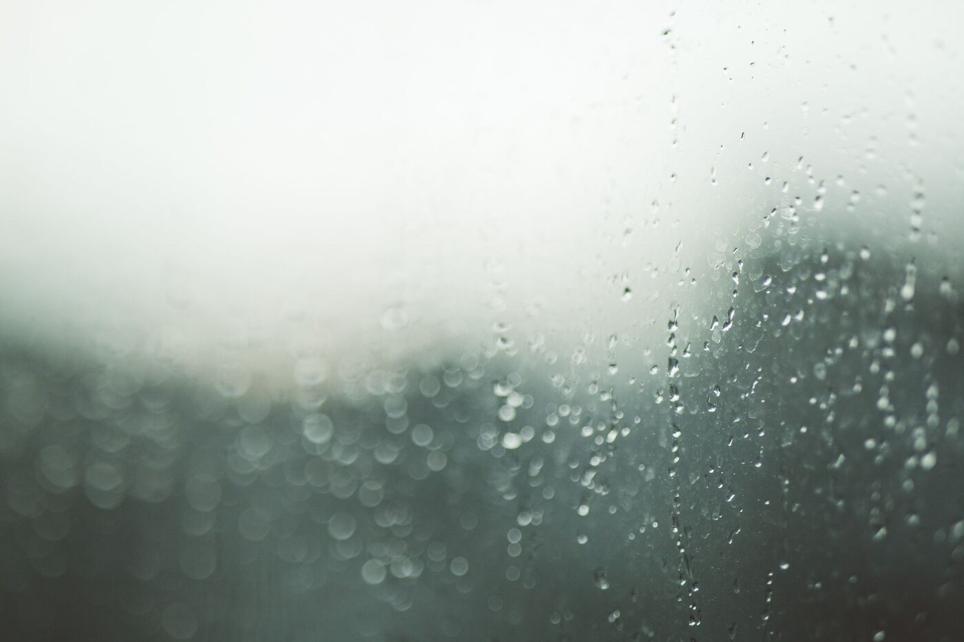 Gouttes de pluie sur une vitre, arrière-plan vert flou, lumière grise