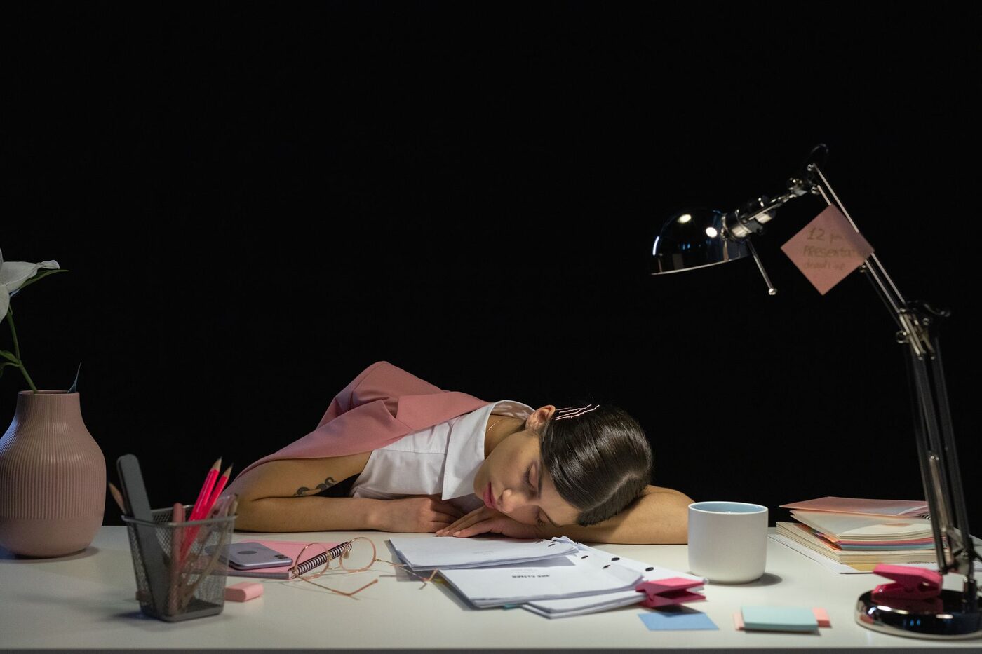 Personne endormie sur un bureau encombré, lampe allumée tard le soir