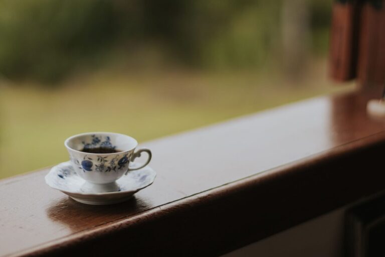 Tasse de thé posée sur un rebord de fenêtre en bois, jardin flou derrière la vitre