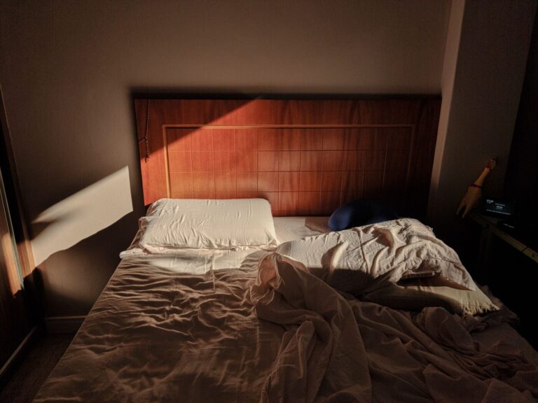 Lit défait au petit matin, draps froissés, lumière chaude entrant par la fenêtre